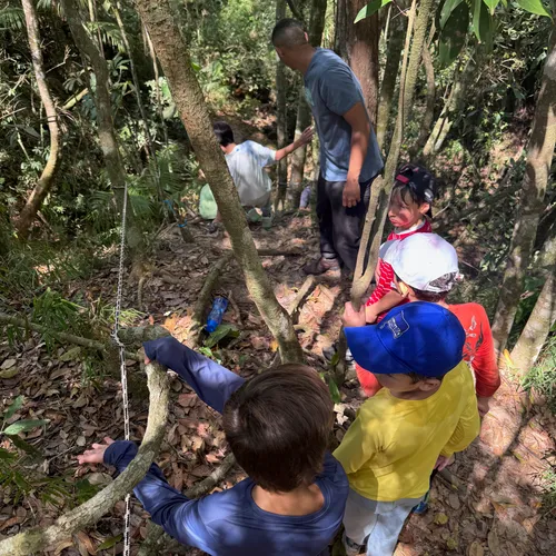 Guia e crianças atravessando a mata fechada segurando uma corda-guia na trilha